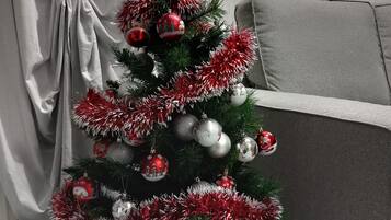 Árvore de Natal com enfeites e guirlanda, em um quarto com sofá cinza e cortinas.