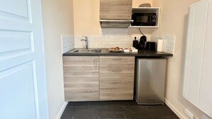 A compact kitchen with a built-in microwave, a stainless steel refrigerator, and a sink with a modern faucet. - Charmant studio terrasse en centre-ville (Châtellerault)