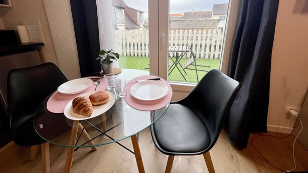 A dining area with a glass table, two chairs, and a view of a fenced backyard through large windows. - Charmant studio terrasse en centre-ville (Châtellerault)