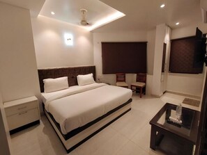 A modern hotel room with a large bed, a desk with a chair, a TV, and a ceiling fan. - HOTEL TEMPLE VIEW (Varanasi)