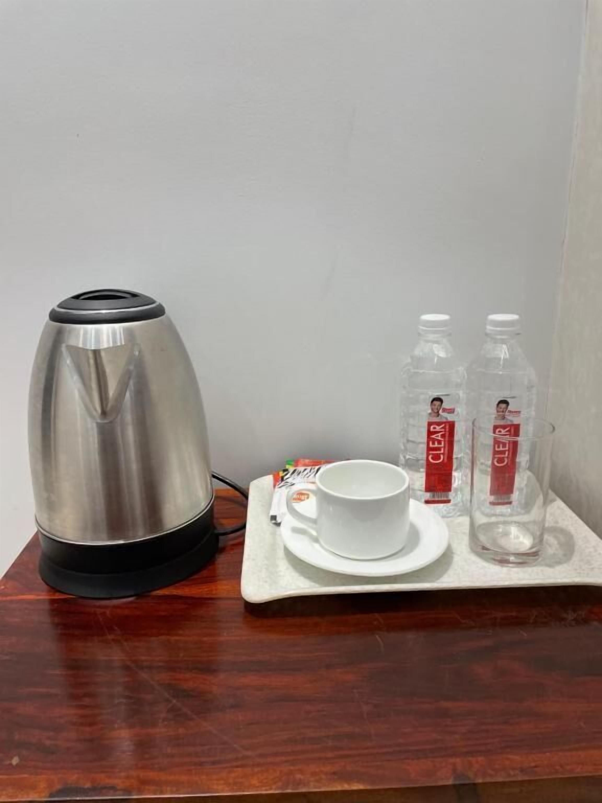 Une bouilloire en acier inoxydable, une tasse et une soucoupe blanches, et deux bouteilles d’eau transparentes, le tout sur un plateau.