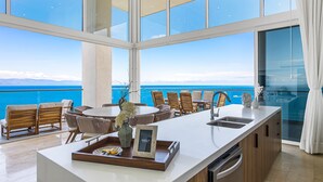A modern kitchen with a large island, a dining area with chairs, and a view of the ocean.