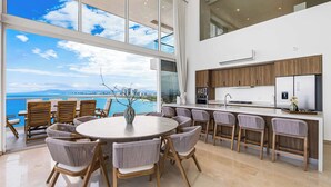 A modern kitchen with a large island, wooden cabinets, and a view of the ocean.