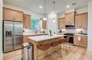 A modern kitchen with stainless steel appliances, wooden cabinets, and a central island with bar stools.