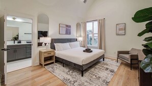 A bedroom with a bed, bedside table, lamp, and a view of the outside.