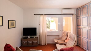 Una habitación con televisión, sofá, silla y ventana con cortinas.