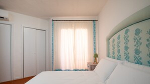 Un dormitorio con una cama grande, una mesita de noche con lámpara, una ventana con cortinas y un armario.