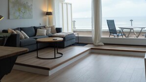 A modern living room with a sofa, a coffee table, and a view of the ocean through large windows.