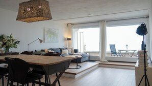 A modern living room with a dining area, a sofa set, and a large window with a view.