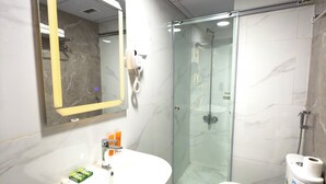 Casa de banho moderna com lavatório de mármore, cabine de duche com vidro e sanita com dispensador de papel.