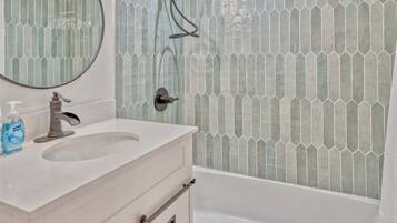 A bathroom with a white vanity, a mirror, a shower with a glass door, and hexagonal patterned tiles.