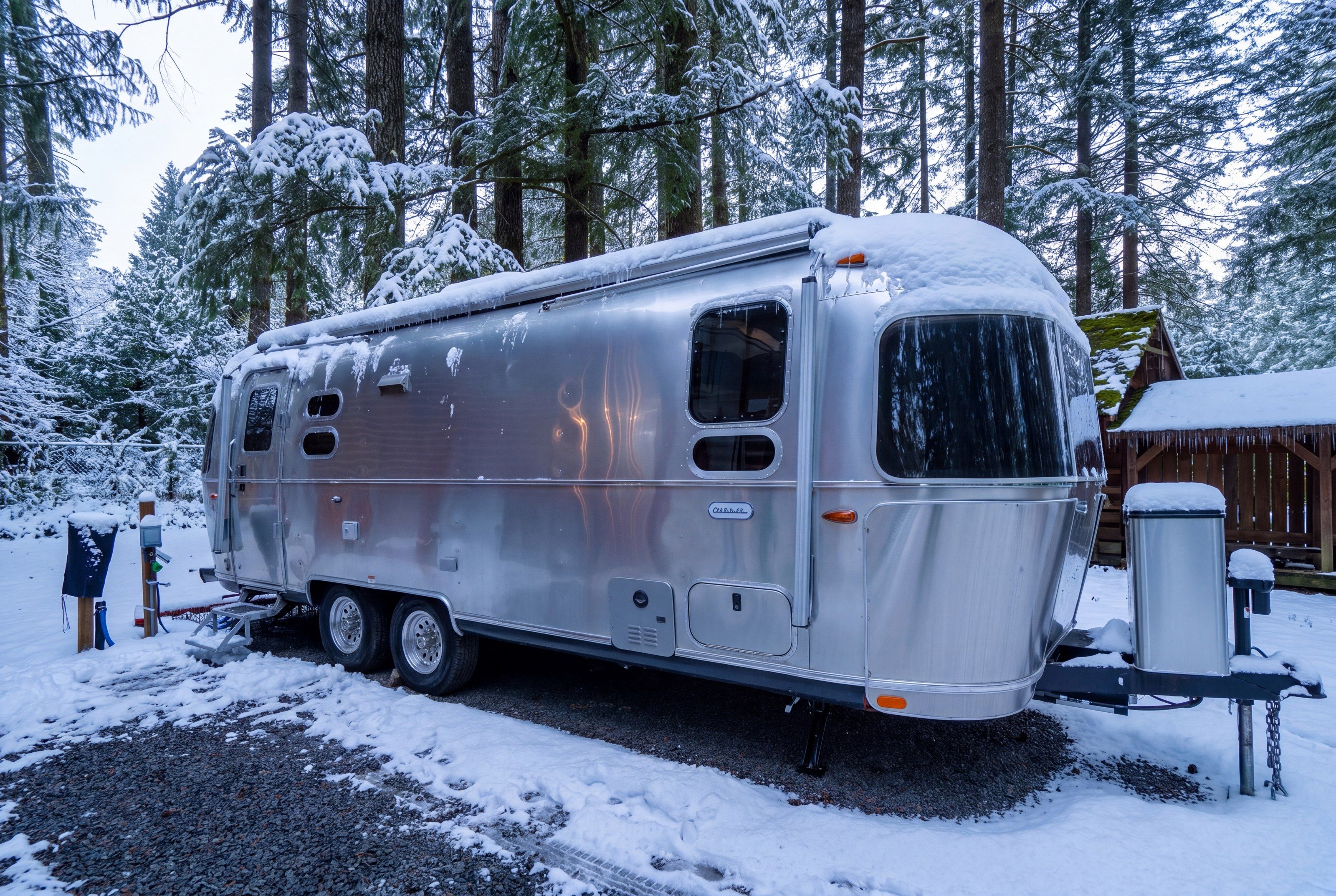 A silver RV parked in a snowy forest.