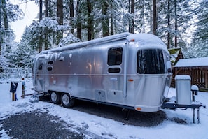 A silver RV parked in a snowy forest. - Winter Log Cabin Compound • 2 Hot Tubs • Sleeps 14 (Mount Hood Village)