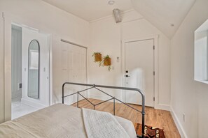 Une chambre à coucher avec un lit, une porte blanche, une fenêtre et une plante accrochée au mur.