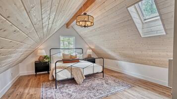A bedroom with a sloped ceiling, a bed with a metal frame, a patterned rug, and a window.