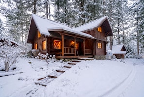 A log cabin with a porch, surrounded by snow-covered trees. - Log Cabin Compound | 6BR/5.5BA | 2 Hot Tubs (Mount Hood Village)