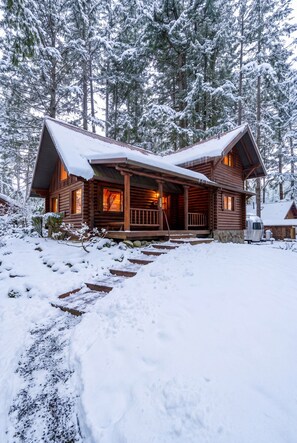 Une cabane en rondins avec un porche, entourée d’arbres couverts de neige.