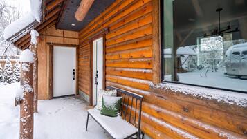 A wooden cabin with a bench and a door, surrounded by snow.