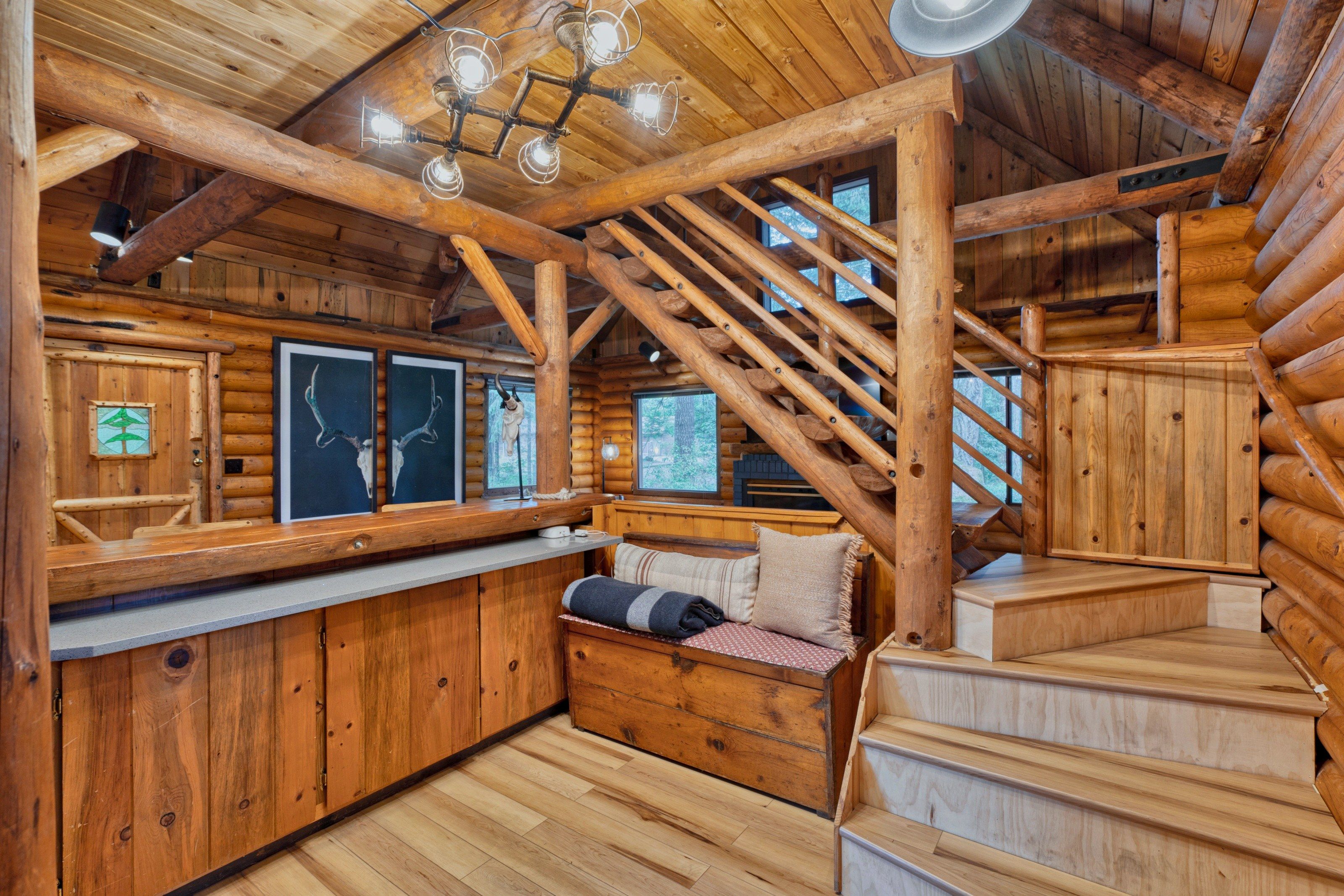 A log cabin interior with a wooden staircase, a bench, and framed pictures on the walls.
