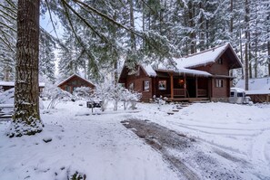 A cabin with a porch, surrounded by snow-covered trees. - Log Cabin Compound | 6BR/5.5BA | 2 Hot Tubs (Mount Hood Village)