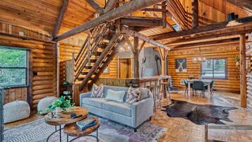 A log cabin interior with a staircase, a sofa, a dining table, and a fireplace.