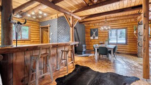 Een rustiek interieur van een blokhut met een bar, een eethoek en een groot zwart leren tapijt.