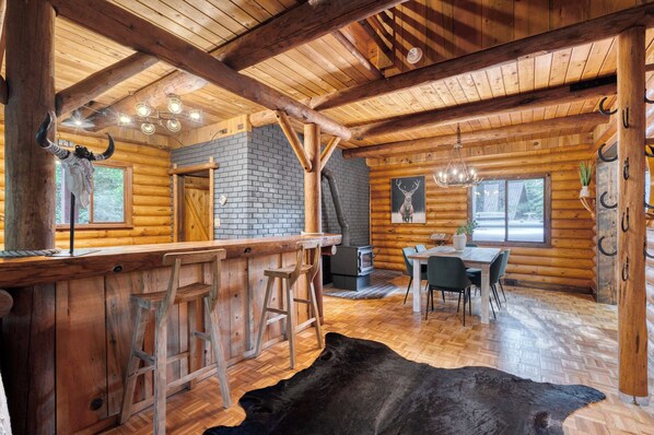 A rustic log cabin interior with a bar area, dining space, and a large black cowhide rug. - Log Cabin Compound | 6BR/5.5BA | 2 Hot Tubs (Mount Hood Village)