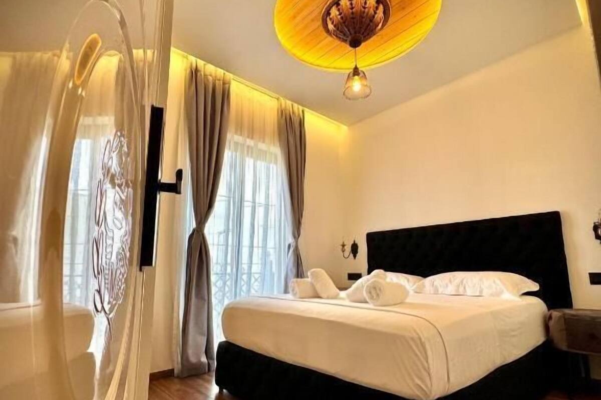 A modern bedroom with a large bed, wooden flooring, and a unique ceiling light fixture.