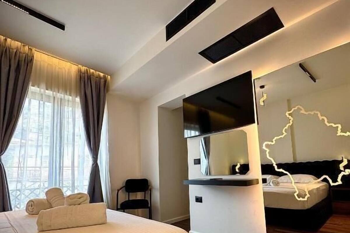 A modern hotel room with a large bed, a desk, and a mirror reflecting the room.