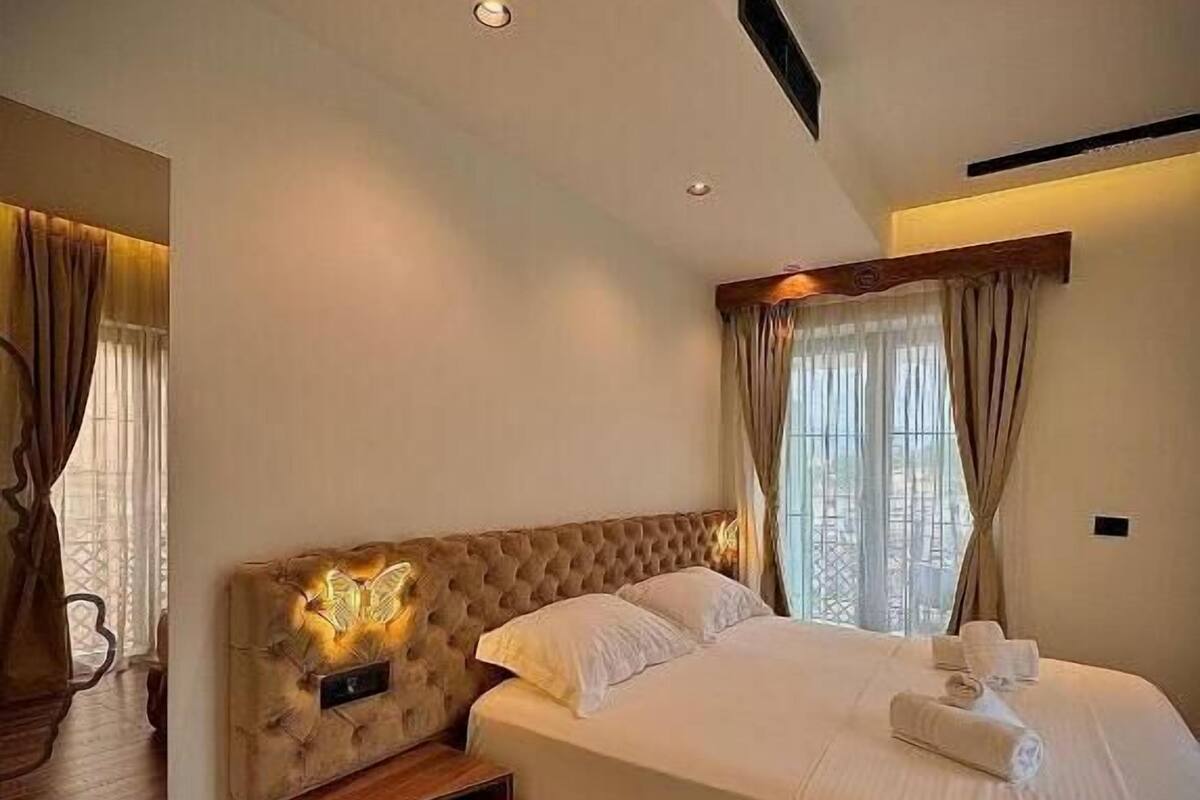 A bedroom with a large bed, wooden flooring, and a wall-mounted light fixture.