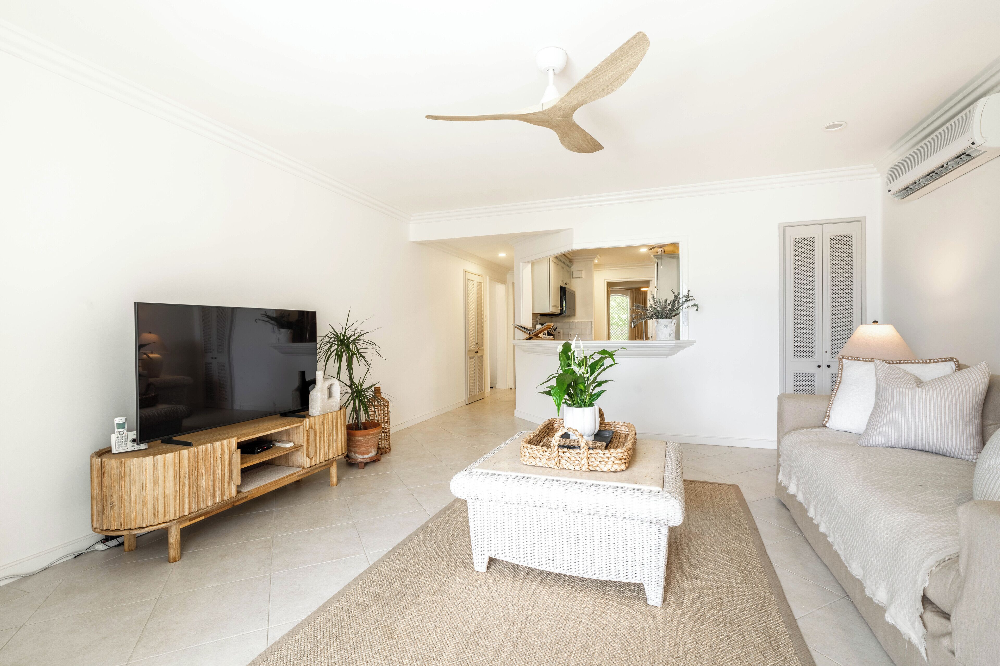 Una sala moderna con una televisión de pantalla plana, mueble de madera para entretenimiento, sofá blanco y ventilador de techo.