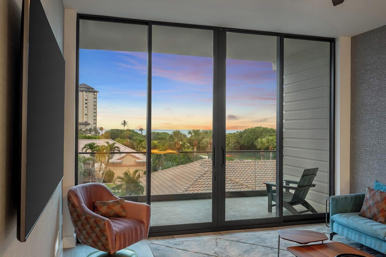 A modern living room with a large sliding glass door leading to a balcony with a city view.