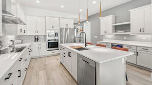 A modern kitchen with white cabinetry, stainless steel appliances, and a central island with a sink and seating.