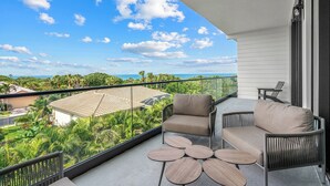 A balcony with two chairs and a small table, overlooking a lush green landscape and a clear blue sky.