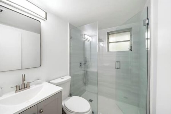 A modern bathroom with a glass shower enclosure, a white sink, and a toilet. - Coconut Cottage in the Grove-Yellow Cottage (Miami)