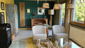 Ein gemütliches Wohnzimmer mit zwei grauen Sesseln, einem Couchtisch aus Holz und einem Glastisch. Ein Kamin mit hölzernem Sims, ein Spiegel und eine Pendelleuchte sind ebenfalls vorhanden.