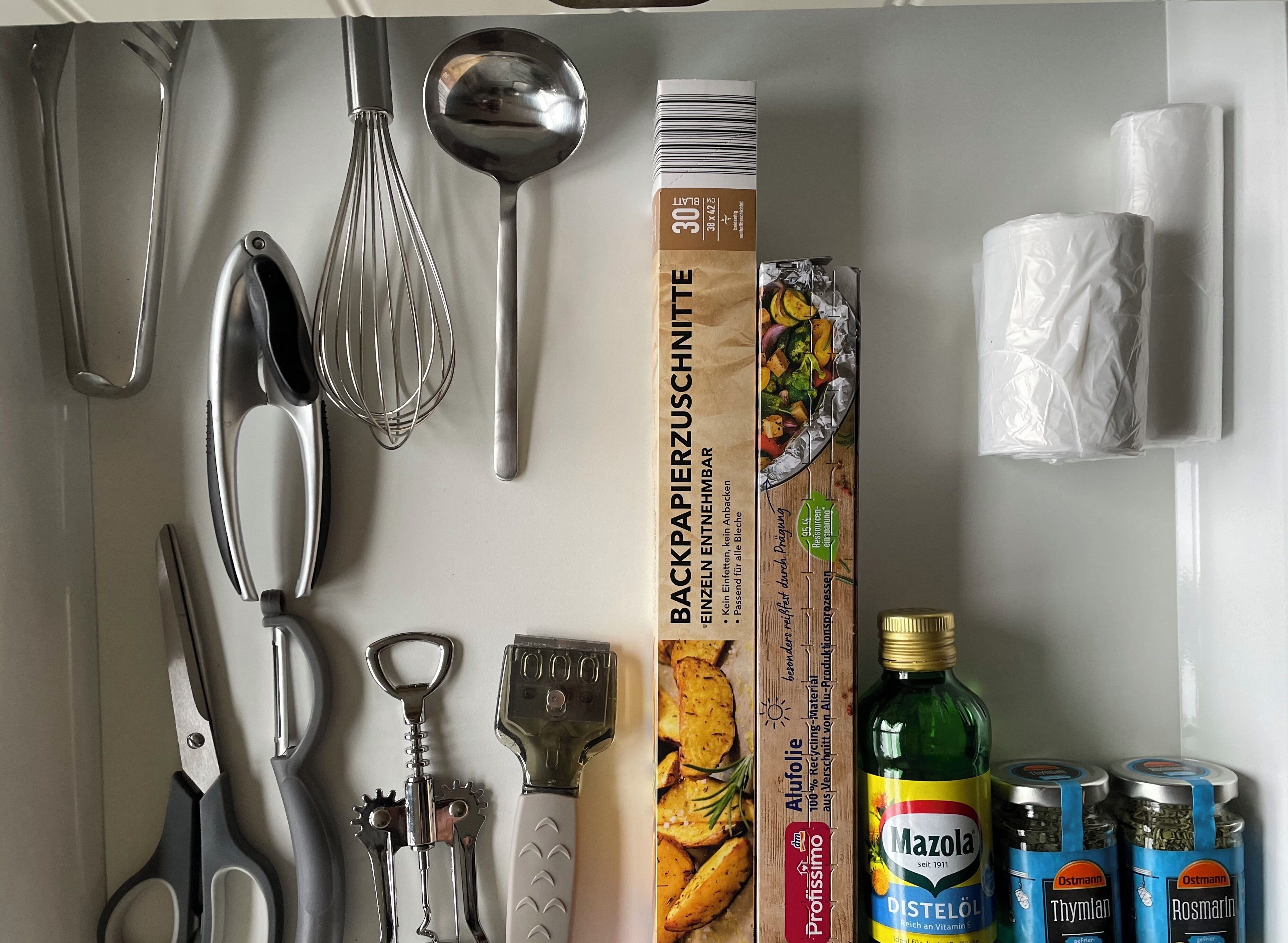A kitchen with various utensils, a whisk, a spatula, a bottle of Mazola oil, and jars of herbs.