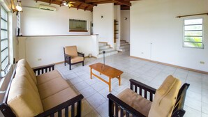 Un vaste espace de vie doté d’un haut plafond, d’un canapé, de deux fauteuils, d’une table basse en bois et d’un escalier menant à un niveau supérieur.