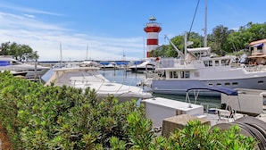 A marina with boats docked, a lighthouse in the background, and lush greenery in the foreground.