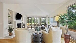 A modern living room with a fireplace, comfortable seating, and large windows offering a view of the outdoors.