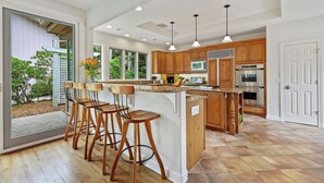 A modern kitchen with wooden cabinets, a large island with bar stools, stainless steel appliances, and a view of the outdoors.