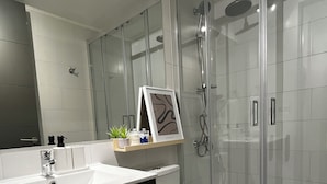 Un baño moderno con cabina de ducha de vidrio, inodoro blanco y tocador con espejo y lavamanos.