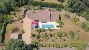 Vista aérea de una casa con piscina, rodeada de jardines ajardinados y árboles.