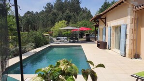Piscina con sillones de descanso, un área de estar techada y vista a un área boscosa.