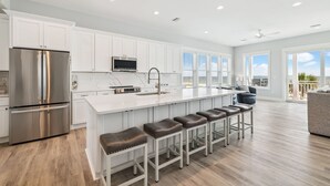 A modern kitchen with white cabinets, stainless steel appliances, and a large island with bar stools. - Large Luxury Beach House with Pool (Port St. Joe)