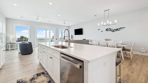 A modern kitchen with a large island, white cabinetry, and a built-in dishwasher. - Large Luxury Beach House with Pool (Port St. Joe)