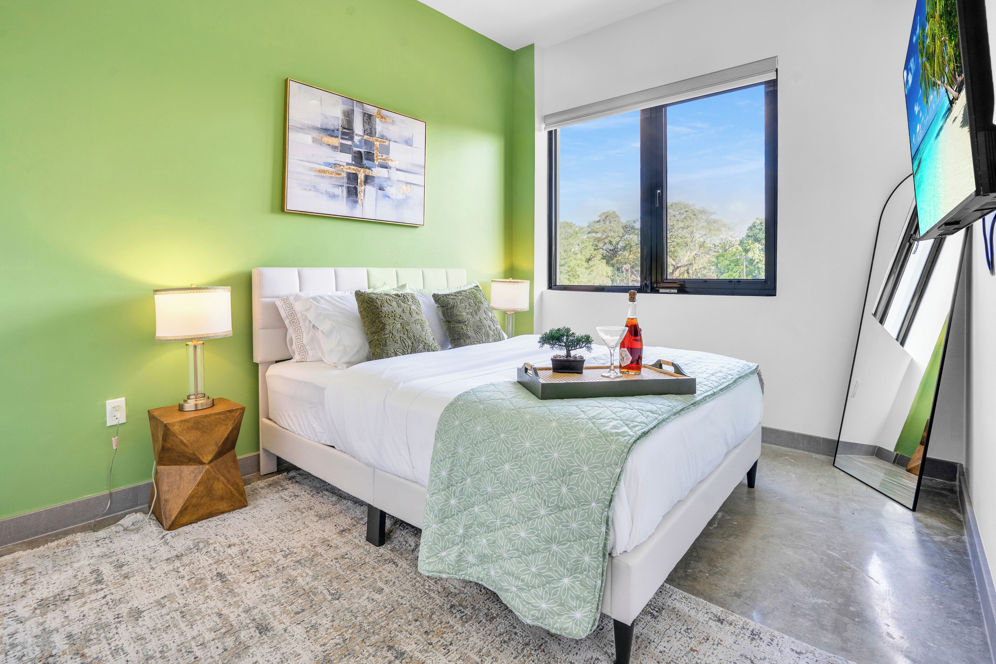 A bedroom with a bed, green walls, a window, a painting, and a nightstand.