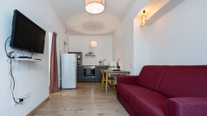 Ein modernes Wohnzimmer mit Flachbildfernseher, einem roten Sofa, einer Küchenzeile mit Esstisch und einer Deckenleuchte.