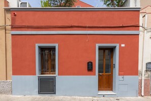 A building with a red facade, two windows with metal grilles, a wooden door, and a small mailbox.