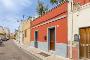 Una calle estrecha con edificios pintados de varios colores, una acera y coches aparcados.